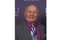  Carl Inzerillo, DO (COM 1964) smiles in a grey suit and purple tie. 